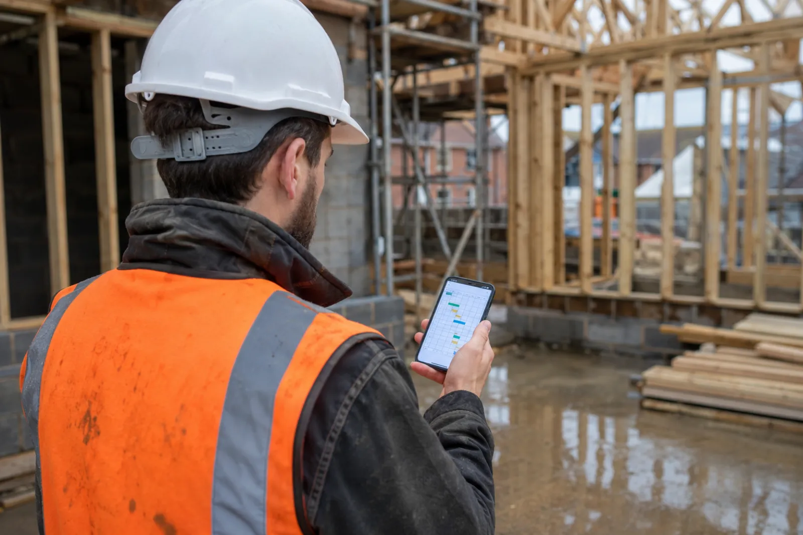 UK site manager checking the short-interval plan on his phone in front of a timber frame new build