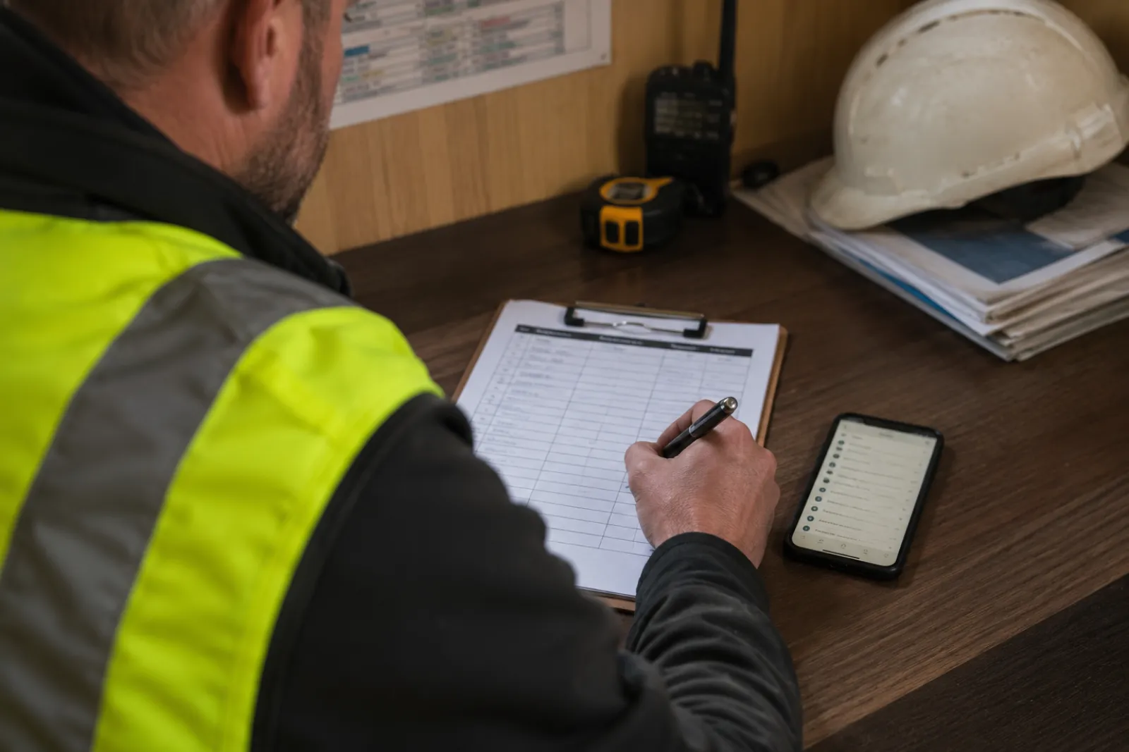 UK site foreman writing the weekly work plan on a clipboard beside a phone showing the task list